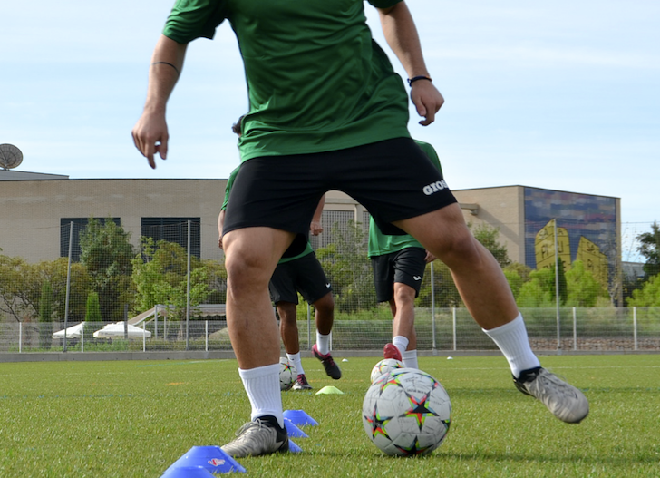 Futbolistas realizando ejercicios técnicos con balón en campo de entrenamiento