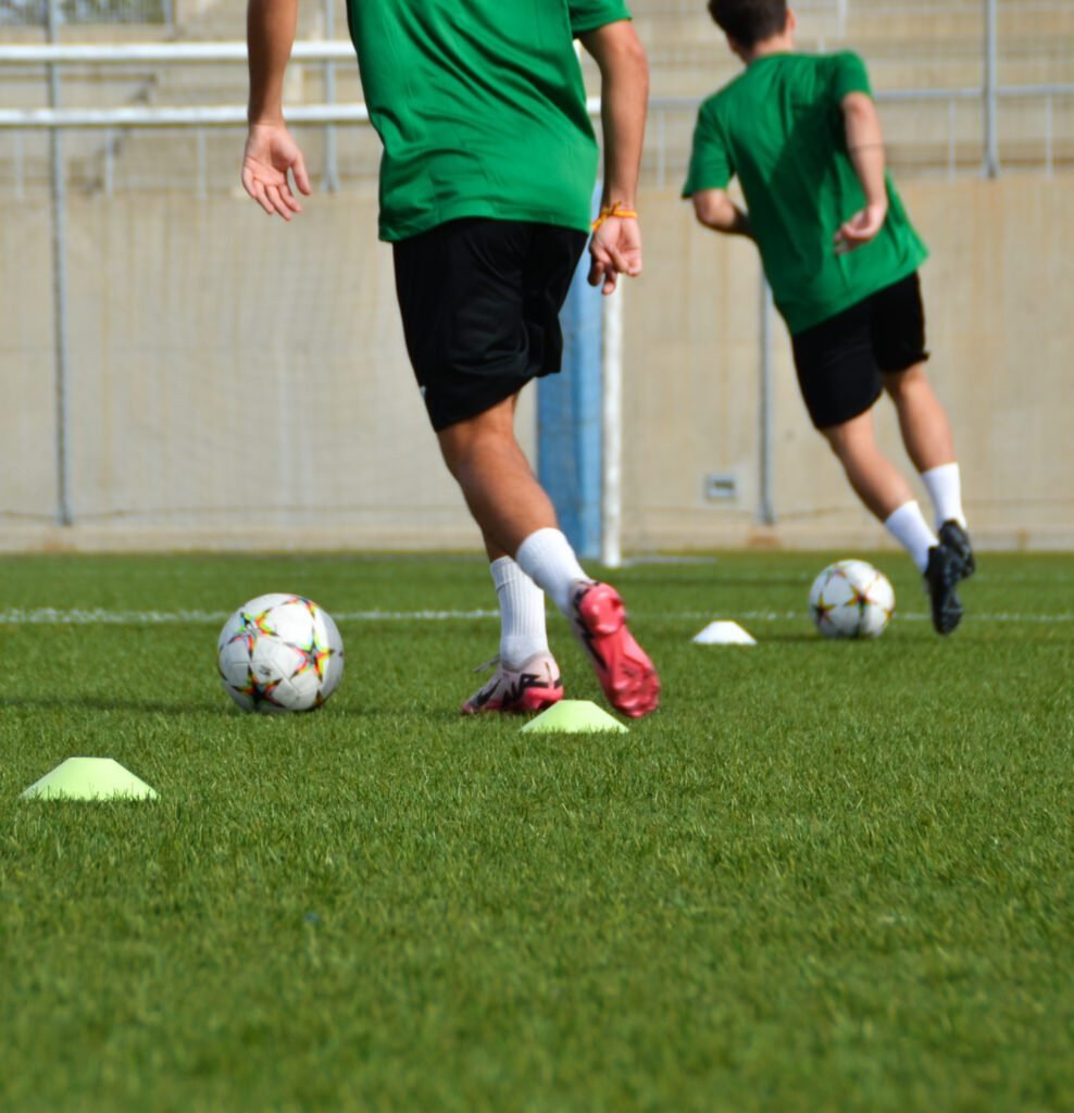 Jugadores realizando ejercicios técnicos con balón y conos durante entrenamiento de fútbol base